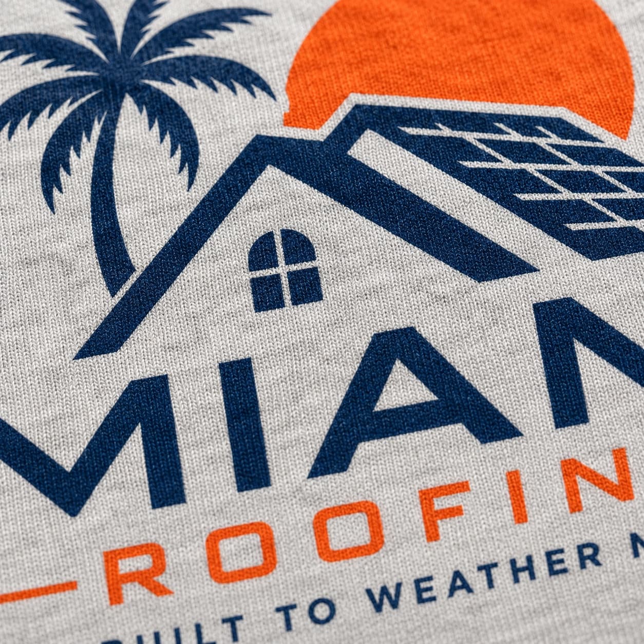Close-up of a screen-printed Miami Roofing company tee on heather grey cotton, with a bold navy and orange logo featuring a palm tree, house, and sun